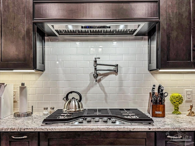 kitchen with stainless steel gas stovetop, dark brown cabinets, light stone countertops, and backsplash