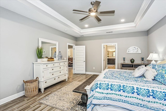 bedroom with a tray ceiling, crown molding, baseboards, and wood finished floors