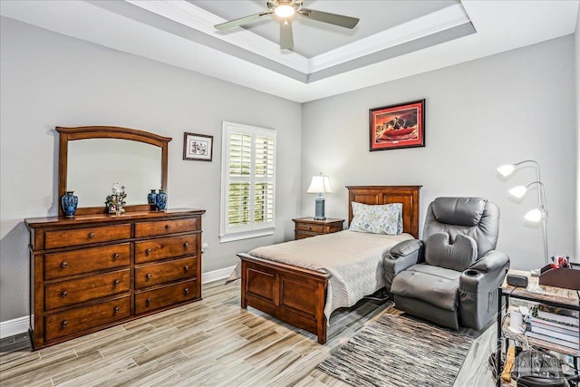 bedroom with light wood finished floors, a ceiling fan, baseboards, a raised ceiling, and ornamental molding