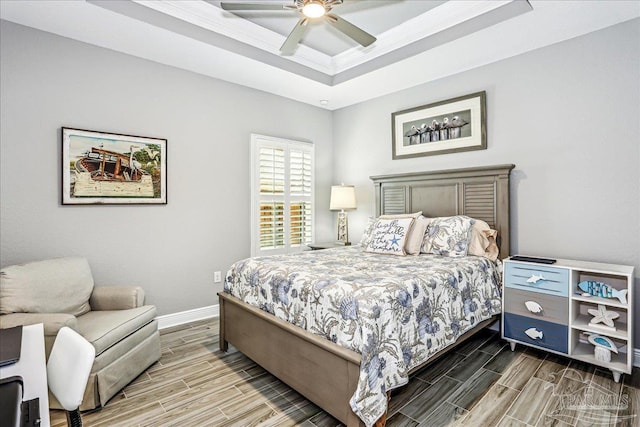 bedroom with a tray ceiling, wood finish floors, baseboards, and a ceiling fan