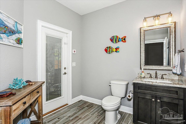 bathroom featuring toilet, baseboards, vanity, and wood finished floors