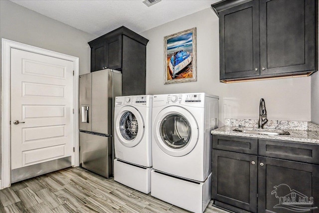 laundry area featuring light wood-style flooring, washing machine and dryer, cabinet space, and a sink