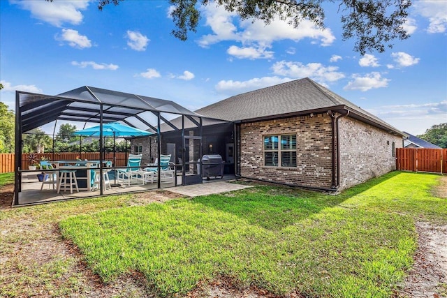 back of house with a lawn, brick siding, a patio area, glass enclosure, and a fenced backyard