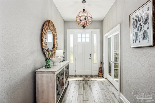 entrance foyer with a chandelier, a textured wall, and light wood finished floors