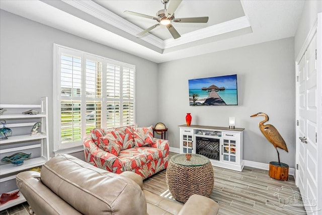 living room with a tray ceiling, wood tiled floor, baseboards, ceiling fan, and ornamental molding