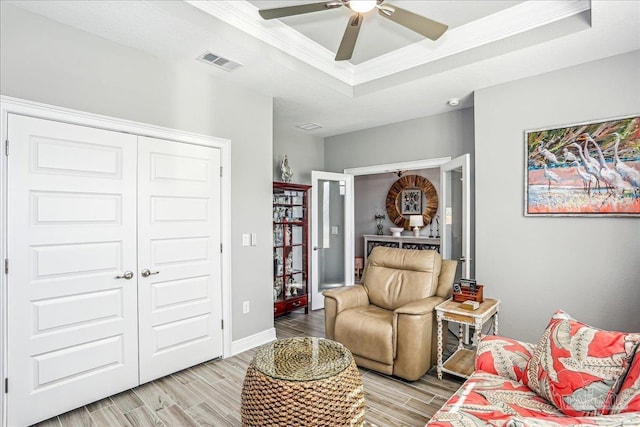 living area with a ceiling fan, wood tiled floor, ornamental molding, visible vents, and a raised ceiling