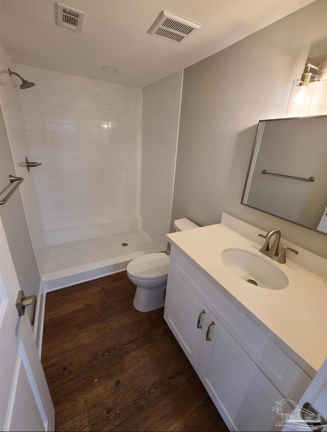 bathroom featuring vanity, a tile shower, hardwood / wood-style flooring, and toilet