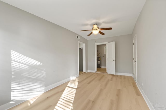 spare room featuring water heater, ceiling fan, and light wood-type flooring