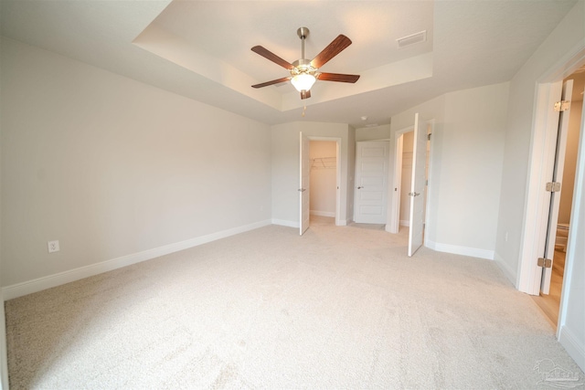 unfurnished bedroom featuring a walk in closet, light colored carpet, a raised ceiling, a closet, and ceiling fan