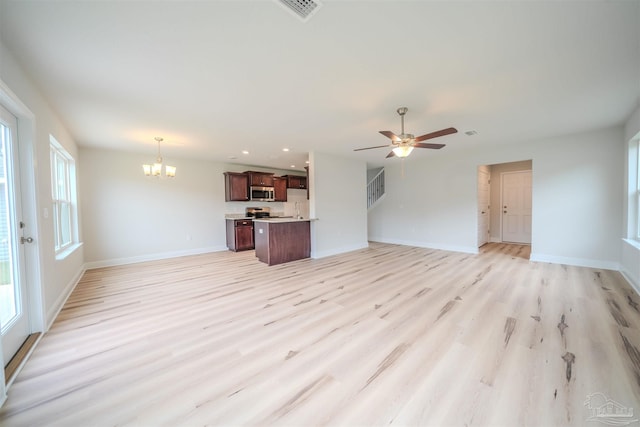 unfurnished living room with ceiling fan with notable chandelier and light hardwood / wood-style floors