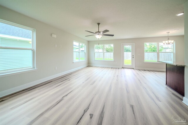 unfurnished living room with ceiling fan with notable chandelier and light hardwood / wood-style flooring