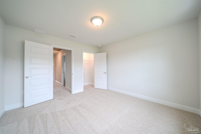 unfurnished bedroom featuring a spacious closet, light carpet, and a closet