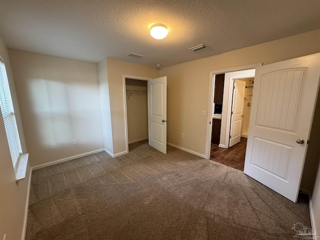 unfurnished bedroom featuring a textured ceiling, visible vents, dark carpet, and a closet