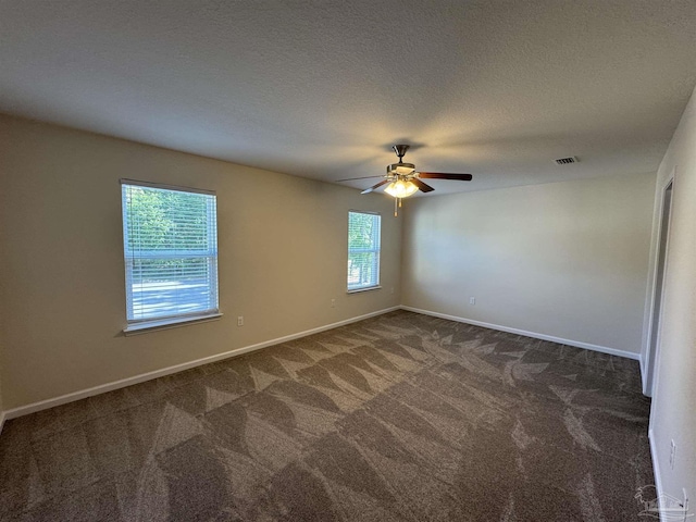 empty room with a textured ceiling, dark colored carpet, a ceiling fan, baseboards, and visible vents