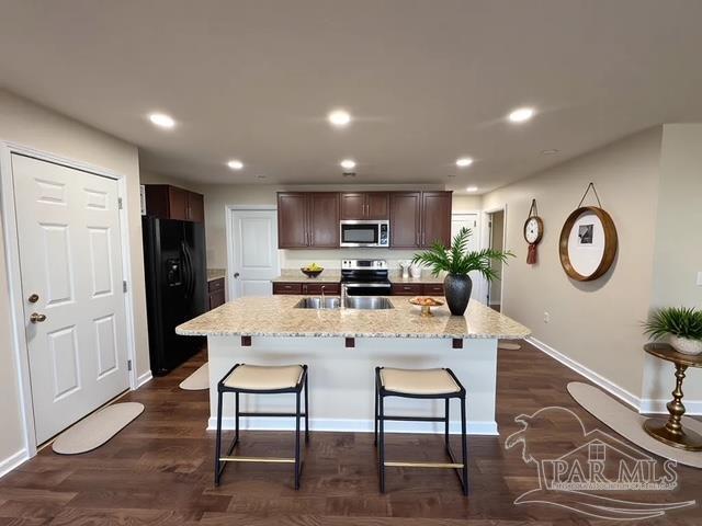kitchen with a sink, a kitchen breakfast bar, dark brown cabinets, and stainless steel appliances