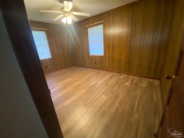 empty room with ceiling fan, wooden walls, and light wood-type flooring