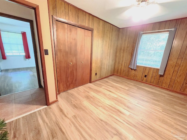 unfurnished bedroom featuring ceiling fan, light hardwood / wood-style floors, a closet, and wood walls