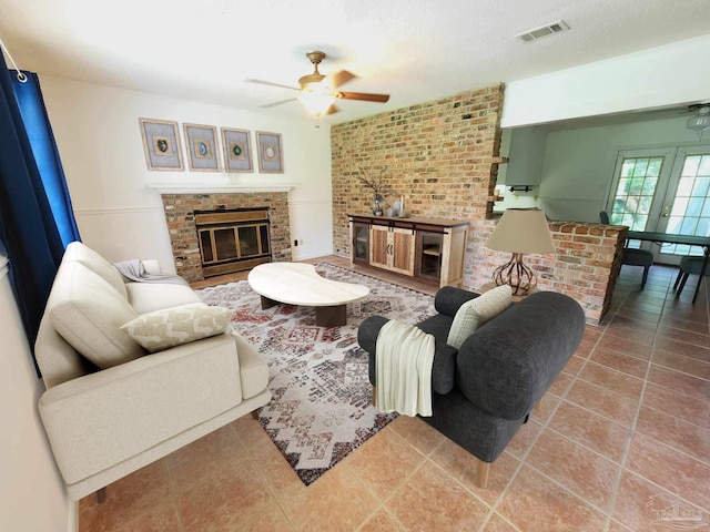 living room featuring tile patterned flooring, ceiling fan, a brick fireplace, and a textured ceiling