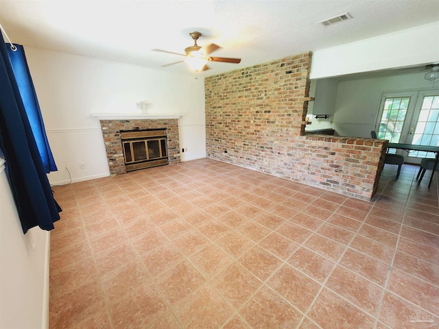 unfurnished living room featuring ceiling fan, brick wall, a textured ceiling, and a fireplace