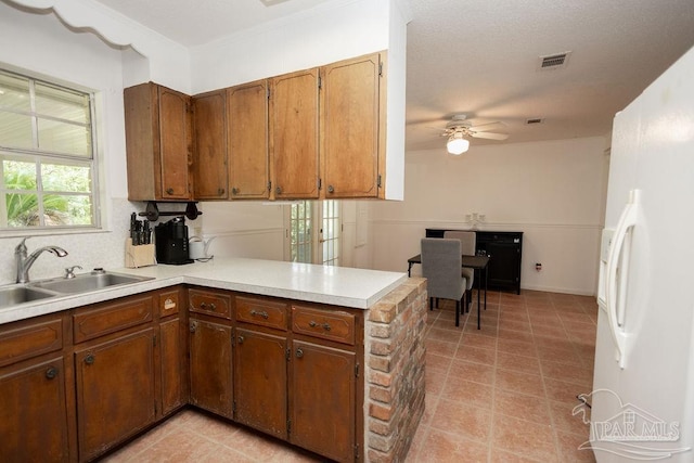 kitchen with sink, light tile patterned flooring, kitchen peninsula, and white fridge