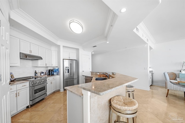 kitchen with under cabinet range hood, high quality appliances, a kitchen breakfast bar, light countertops, and white cabinetry