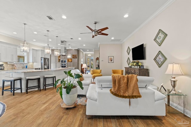 living area with light wood-style floors, visible vents, ornamental molding, and ceiling fan