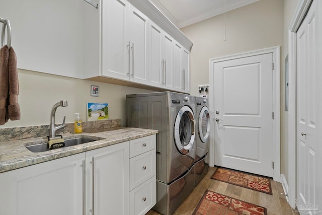 clothes washing area with washing machine and dryer, wood finished floors, a sink, ornamental molding, and cabinet space