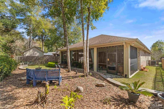 back of property featuring a sunroom, a fenced backyard, a shingled roof, and a yard