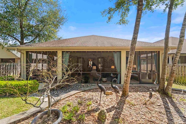 back of house with a sunroom, a shingled roof, and fence