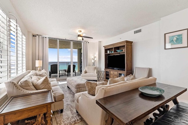 living room with a textured ceiling, ceiling fan, and a wall of windows