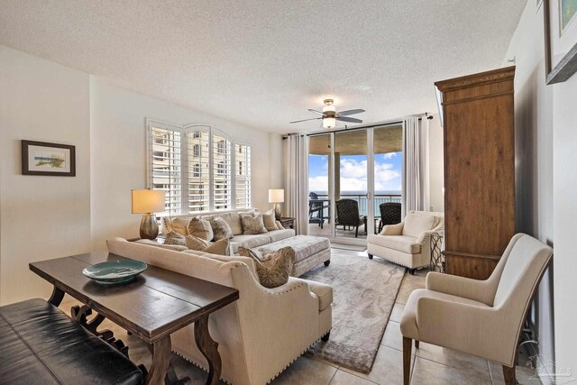 living room with a textured ceiling, ceiling fan, light tile patterned floors, and a wall of windows