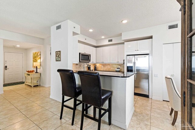 kitchen featuring a breakfast bar area, appliances with stainless steel finishes, kitchen peninsula, decorative backsplash, and white cabinetry