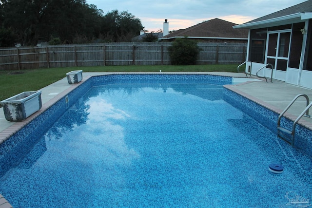 pool at dusk featuring a sunroom and a yard