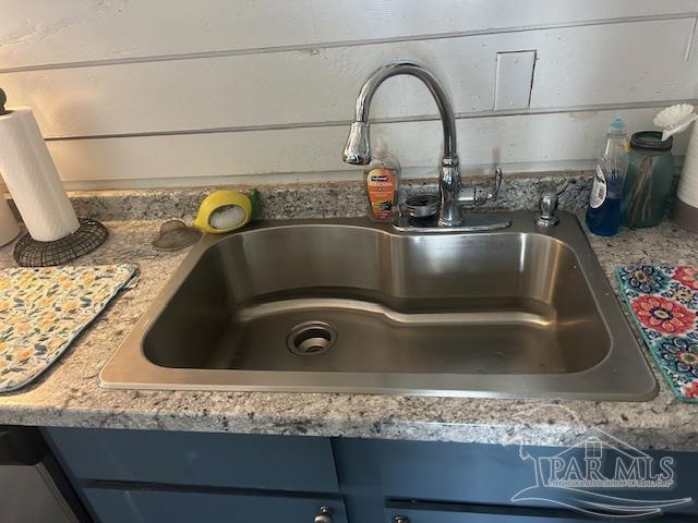 room details featuring blue cabinetry, a sink, and light stone countertops