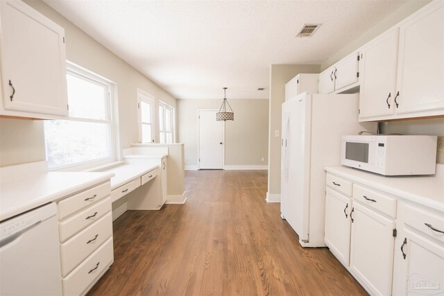 kitchen with white appliances, hardwood / wood-style floors, decorative light fixtures, built in desk, and white cabinets