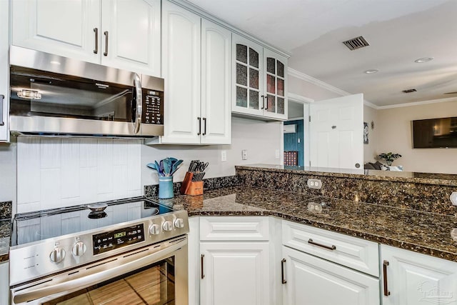 kitchen with white cabinets, stainless steel appliances, crown molding, and dark stone countertops