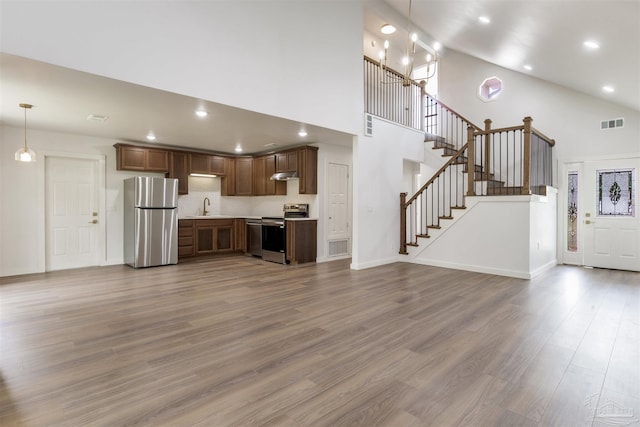 unfurnished living room featuring a sink, high vaulted ceiling, stairs, wood finished floors, and visible vents