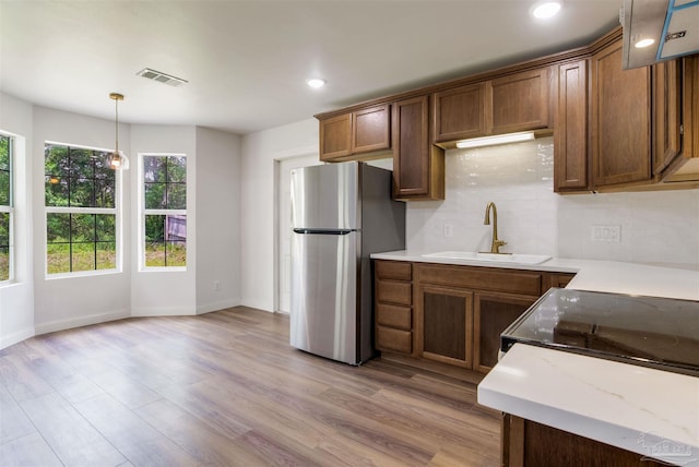 kitchen with decorative backsplash, visible vents, a sink, freestanding refrigerator, and light wood-style floors