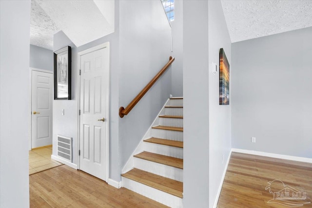 stairway with hardwood / wood-style floors, a textured ceiling, and vaulted ceiling