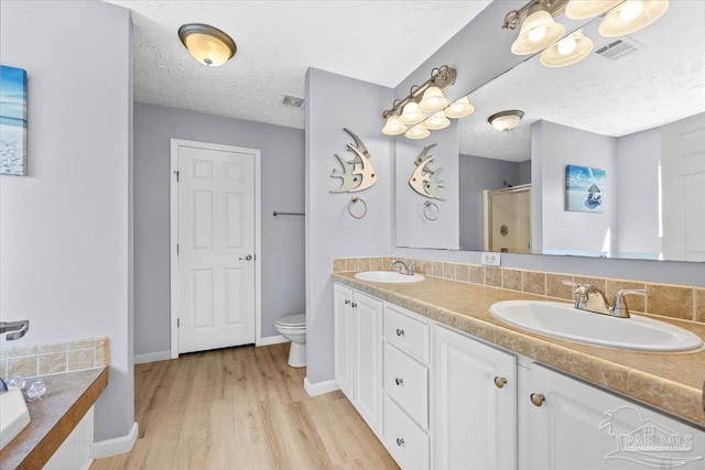 bathroom featuring walk in shower, a textured ceiling, toilet, vanity, and hardwood / wood-style flooring