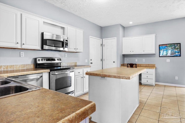 kitchen featuring light tile patterned flooring, white cabinets, a textured ceiling, appliances with stainless steel finishes, and a kitchen island