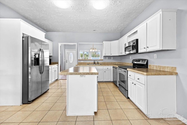 kitchen with appliances with stainless steel finishes, a textured ceiling, a kitchen island, light tile patterned floors, and white cabinetry