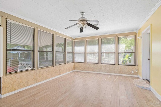 unfurnished sunroom featuring a ceiling fan, ornamental molding, and wood finished floors