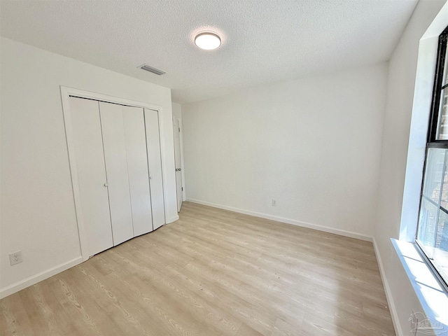 unfurnished bedroom with light wood-type flooring, baseboards, visible vents, and a textured ceiling