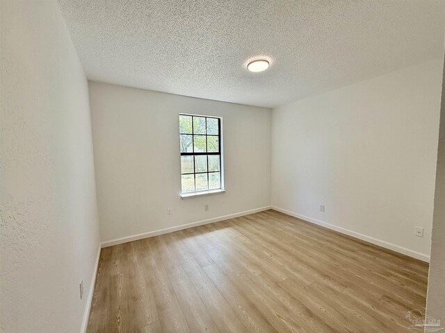 spare room featuring light wood-type flooring, baseboards, and a textured ceiling