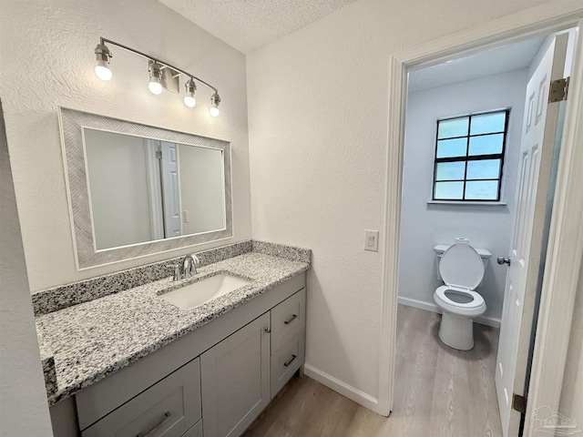 bathroom with baseboards, toilet, a textured ceiling, vanity, and wood finished floors