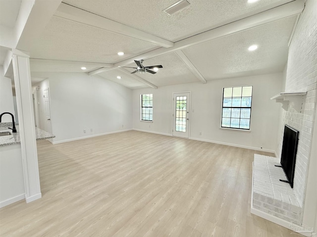 unfurnished living room with visible vents, a brick fireplace, light wood-type flooring, a ceiling fan, and a textured ceiling