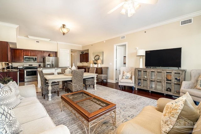 living room with ornamental molding, wood finished floors, visible vents, and a ceiling fan