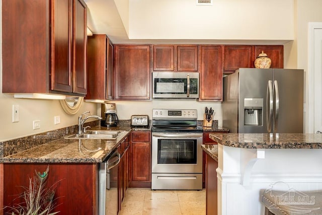 kitchen with stainless steel appliances, dark stone counters, a sink, and dark brown cabinets