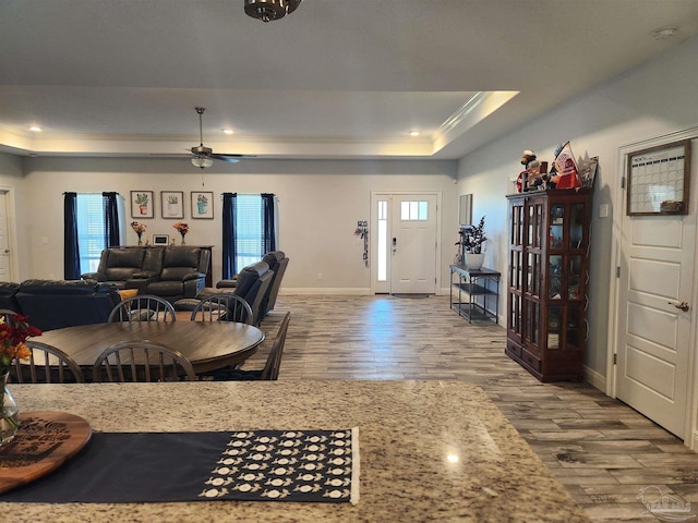 interior space with ceiling fan, plenty of natural light, wood-type flooring, and a tray ceiling